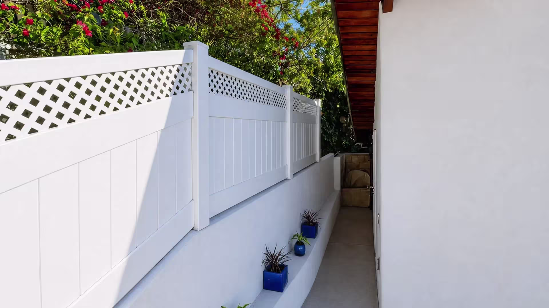 A walkway wall carries a White custom vinyl wall topper beneath dark timber eaves and blue plant pots