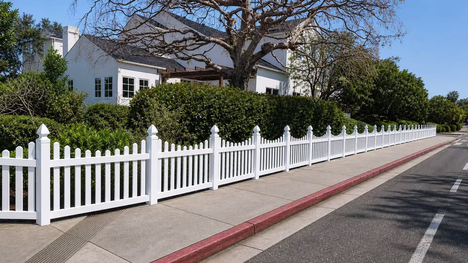 Pickets of the White vinyl dog-ear fence rise above the rail on a diagonal sidewalk run