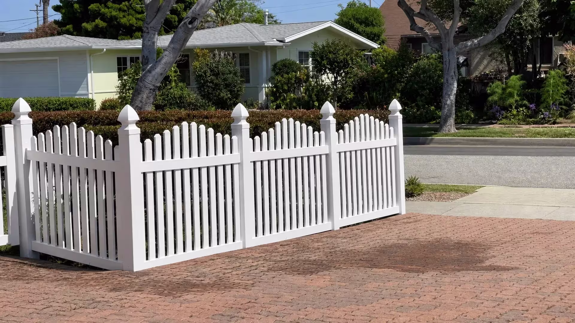Utility wires cross overhead as a White vinyl dog-ear fence recedes past the garage