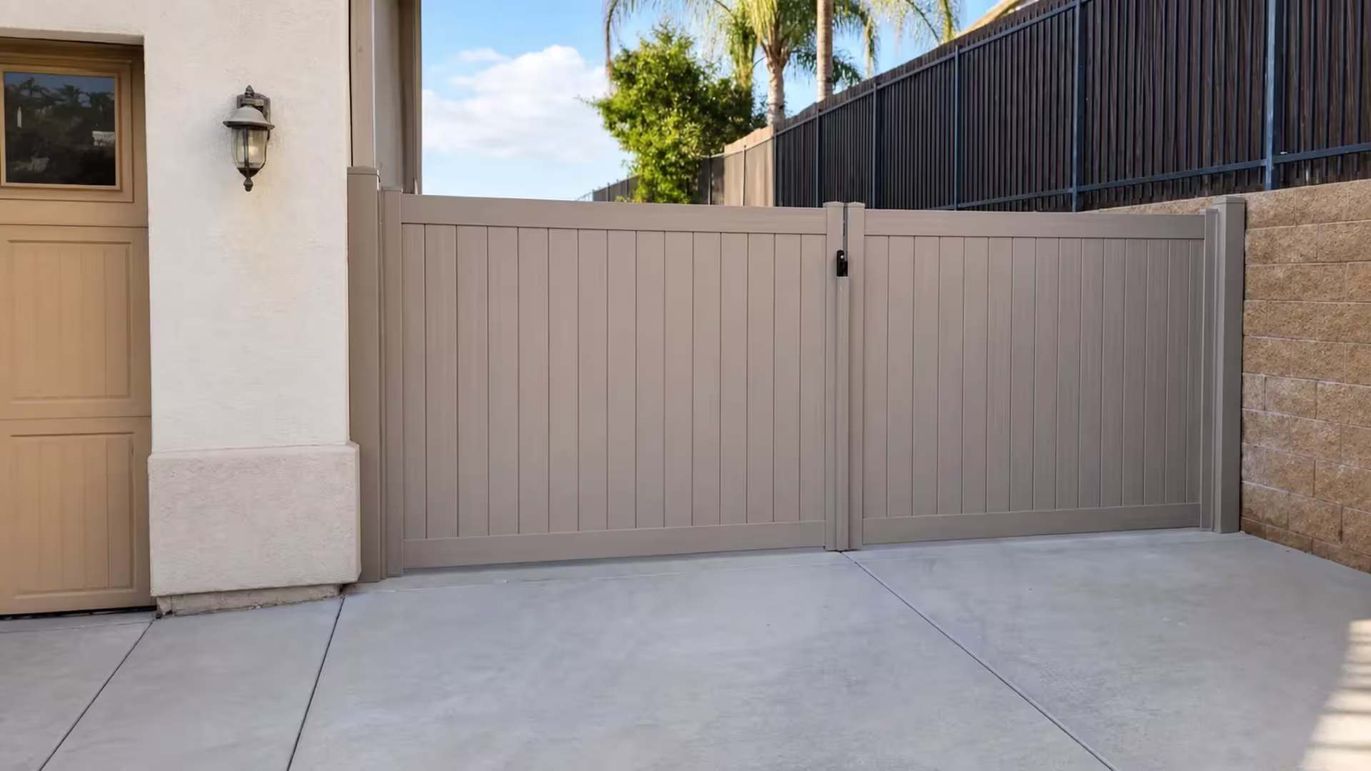 Clay vinyl driveway gate spanning between a stucco house wall and a tan block retaining wall