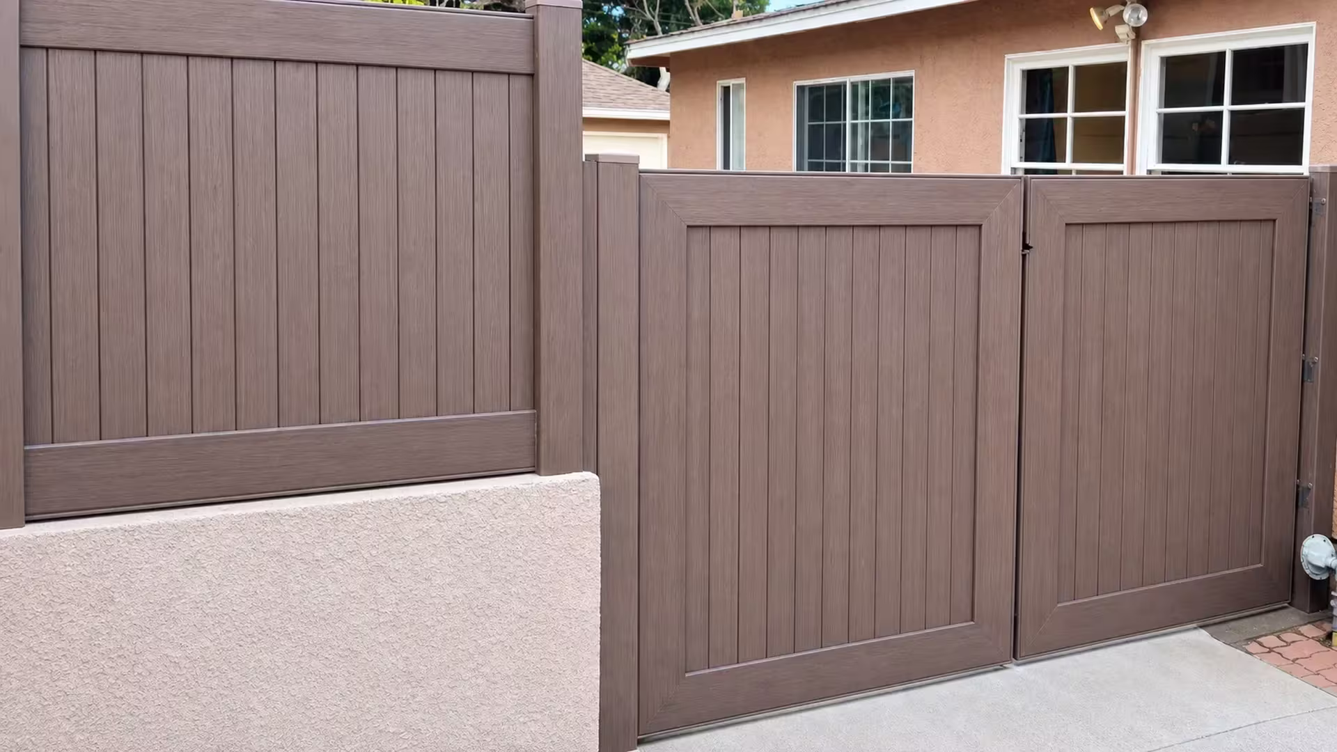 Raised on a peach stucco wall, a fixed privacy panel adjoins this Dark Walnut vinyl driveway gate