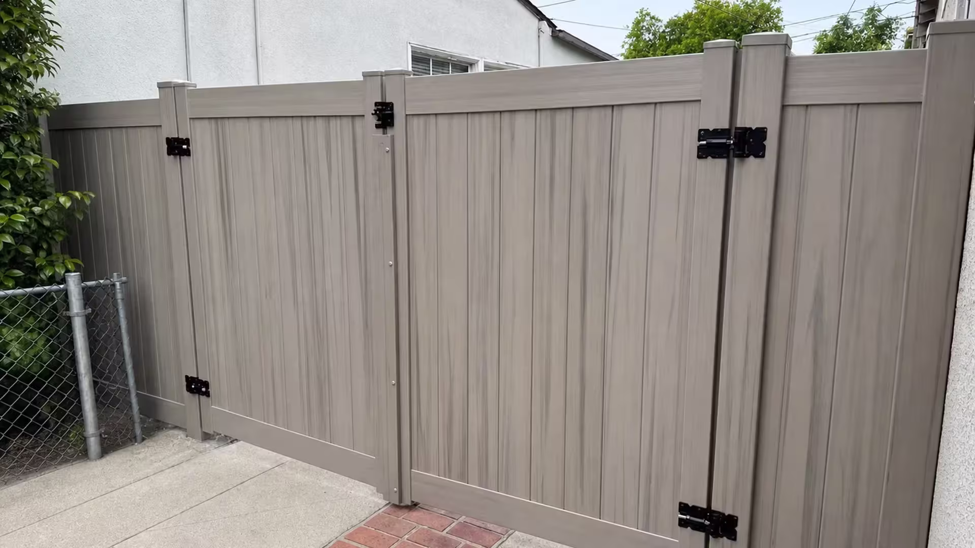 Mesquite vinyl driveway gate with matching square posts standing along a red brick paving strip