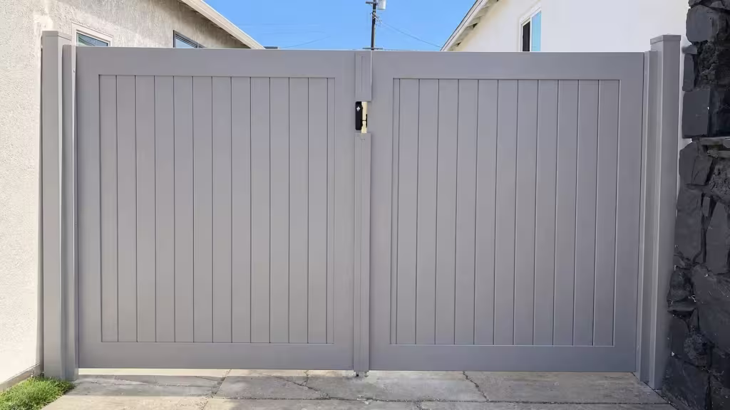 Slate Gray vinyl driveway gate spanning from a stucco building to a dark stone masonry column