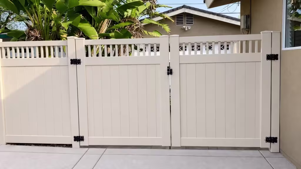 Three framed sections build this Tan vinyl driveway gate standing beside a beige stucco building