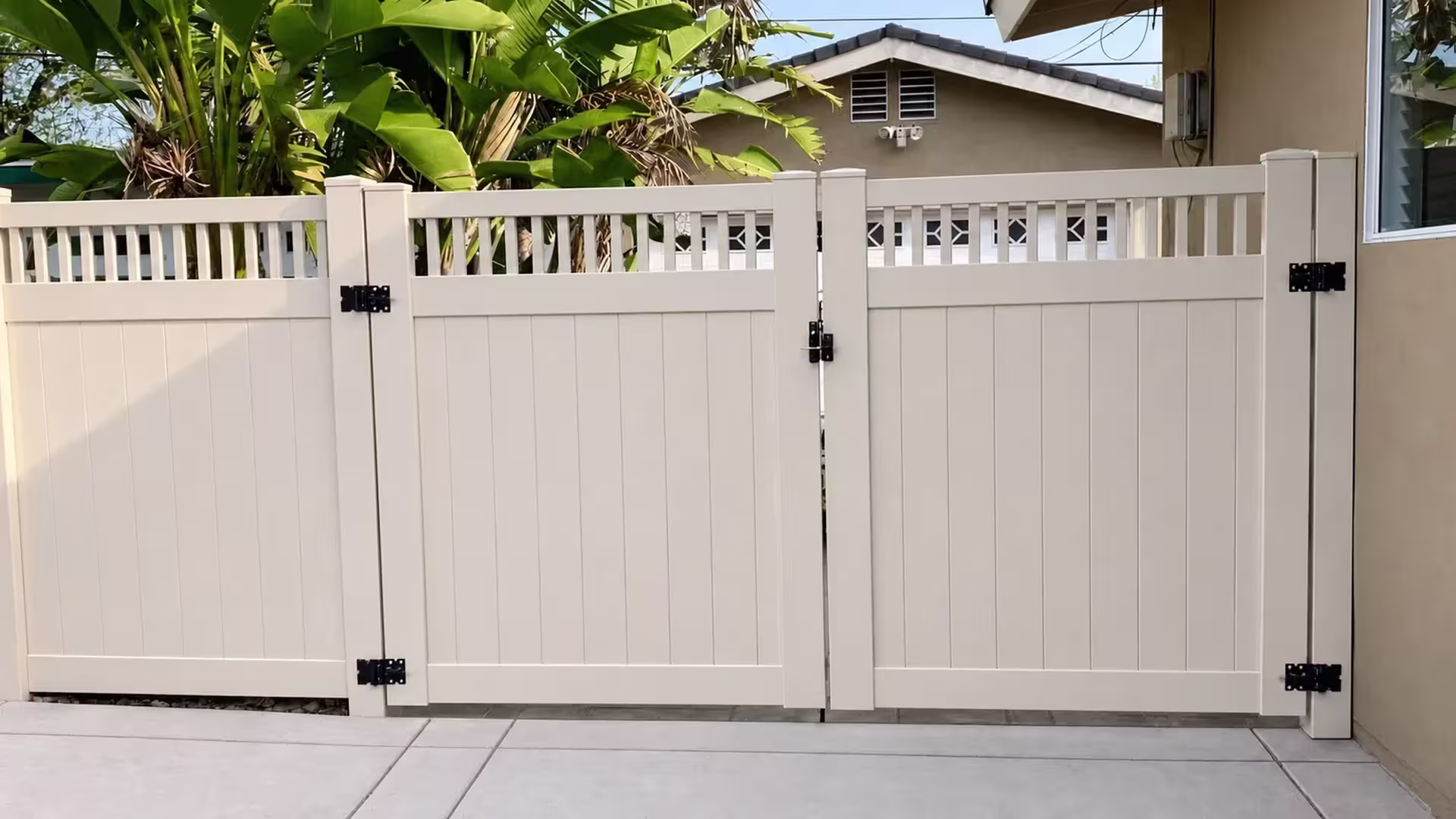 Three framed sections build this Tan vinyl driveway gate standing beside a beige stucco building