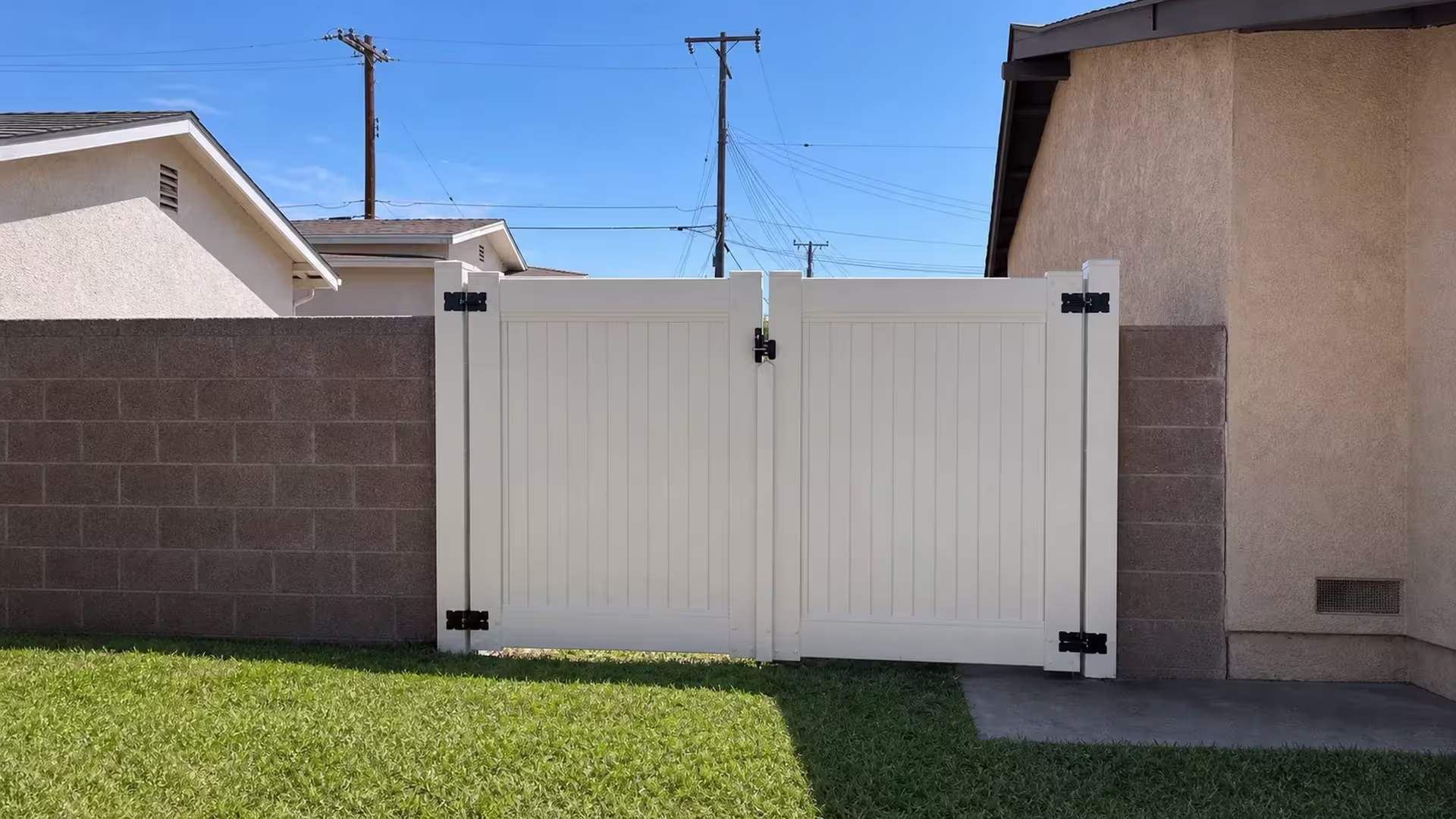 Tan vinyl driveway gate with two equal swinging leaves closing the gap between two masonry walls