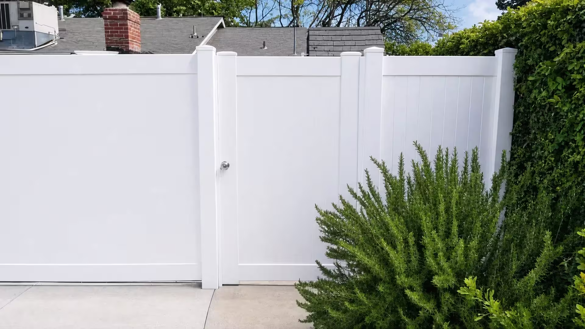 A single vinyl leaf closes this White driveway gate among rosemary shrubs beneath a brick chimney