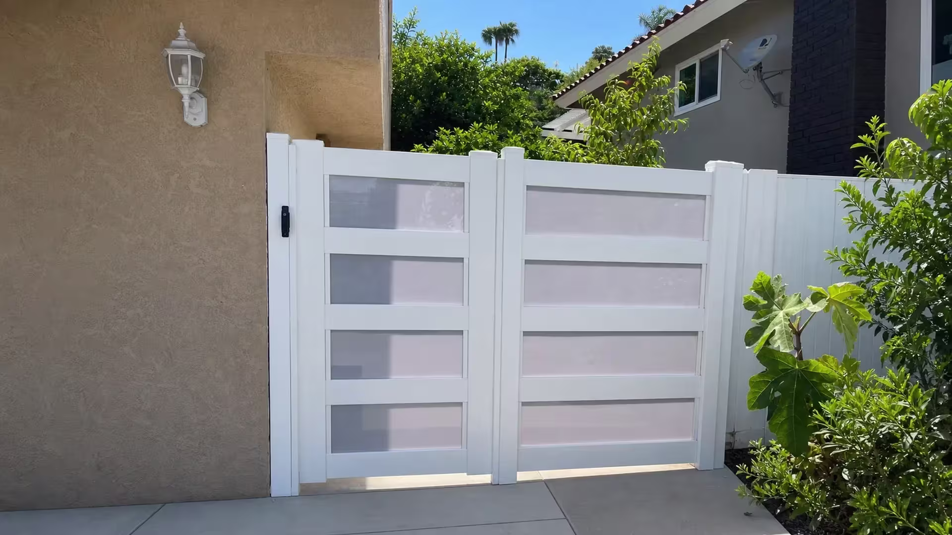 A satellite dish tops one stucco residence beside this White vinyl double driveway gate