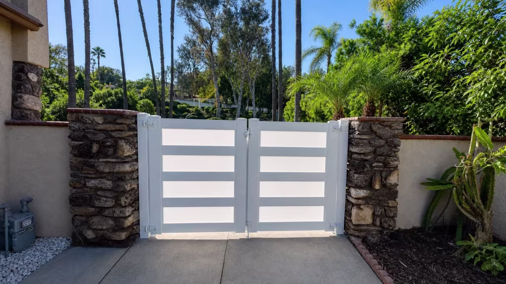 Rough-stone masonry columns anchor this White vinyl double driveway gate beside a planted brick-edged bed
