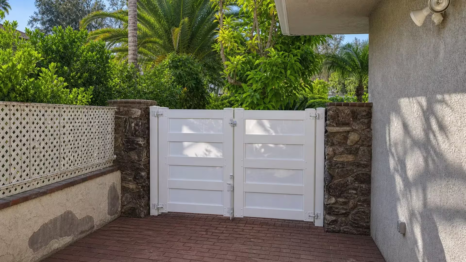 A White lattice fence panel adjoins this vinyl double driveway gate between dark stone columns