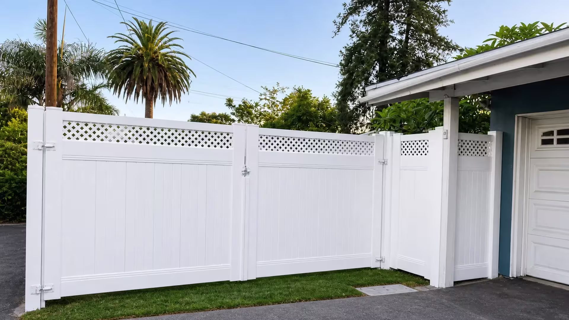 A blue garage door stands beside this lattice-top White vinyl driveway gate and its matching return fence