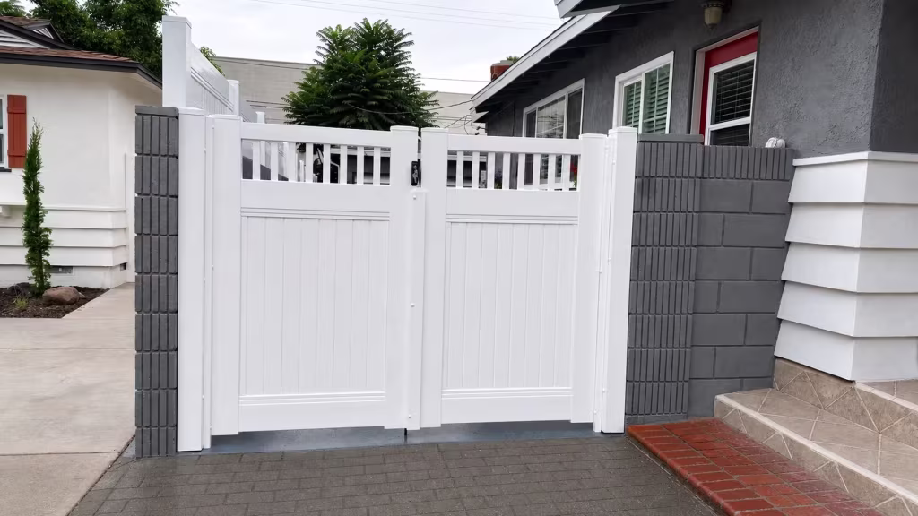 A flight of steps sits beside this White vinyl double driveway gate between gray masonry walls