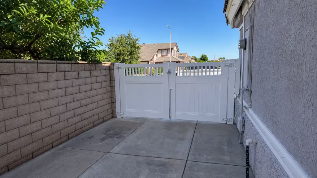 A concrete side drive passes through this White vinyl double driveway gate between a block wall and stucco house