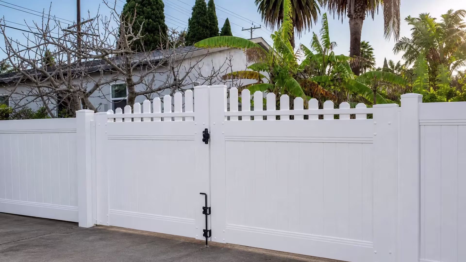 Banana plants and tall evergreens surround this pointed-picket White vinyl driveway gate