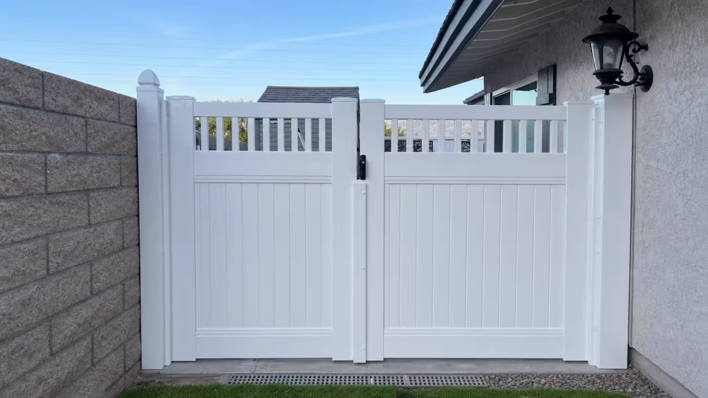 A black wall lantern hangs beside this White vinyl driveway gate, its picket top open above solid privacy boards