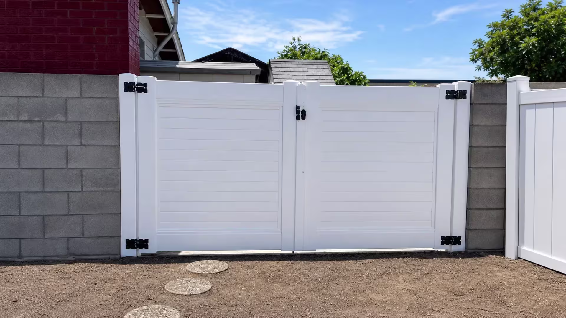 Round stepping-stones lead up to this White vinyl driveway gate, its two leaves meeting between gray block walls