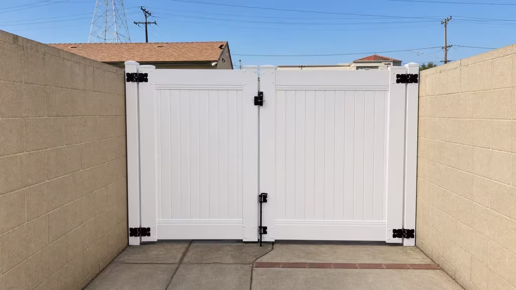 A distant transmission tower rises beyond this White vinyl driveway gate set between two painted masonry walls
