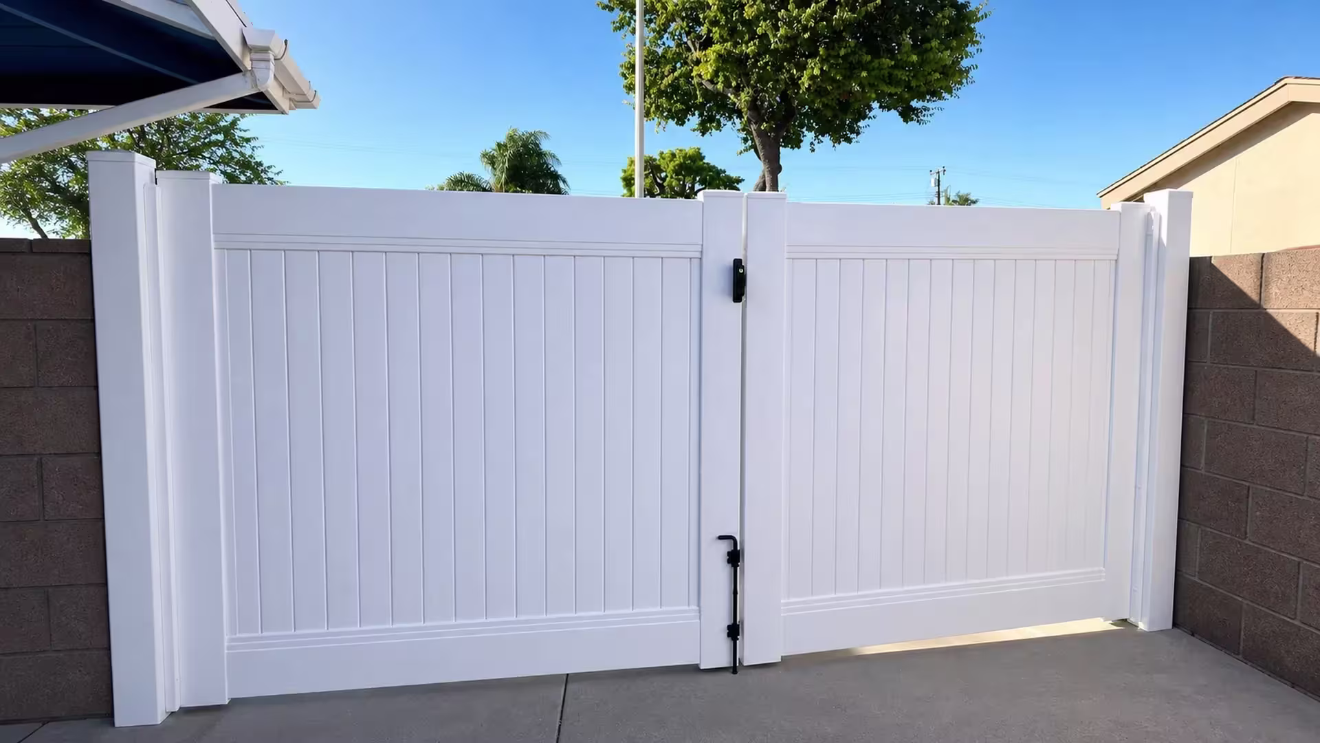 Beneath the house eaves, this White vinyl driveway gate carries unequal leaves with a narrow transition rail above the boards