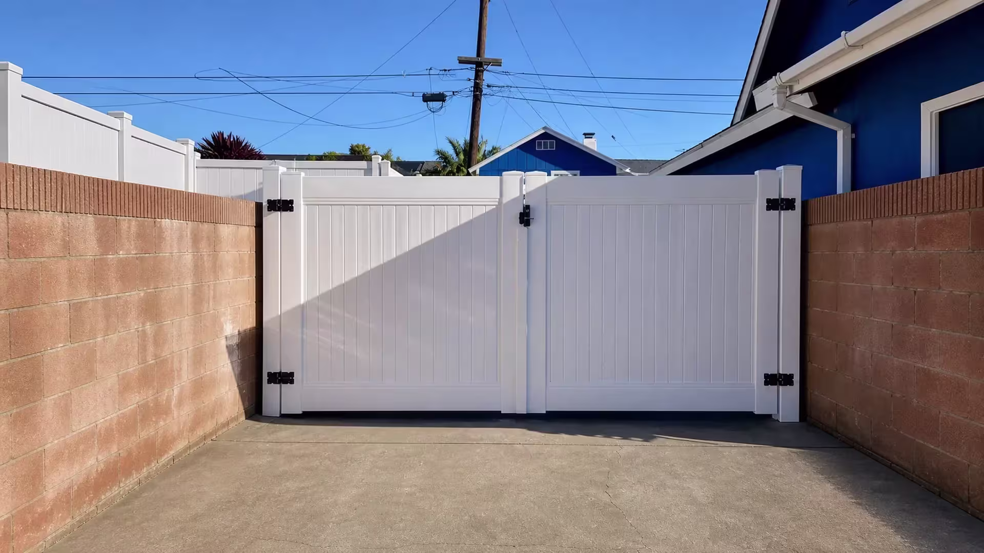 Matching fence returns flank this White vinyl driveway gate, closing the run along masonry walls on both sides