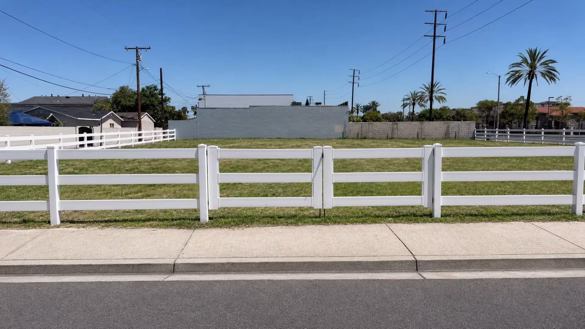 Diagonal metal braces reinforce this White vinyl three-rail ranch driveway gate, standing across from a vacant grassy lot