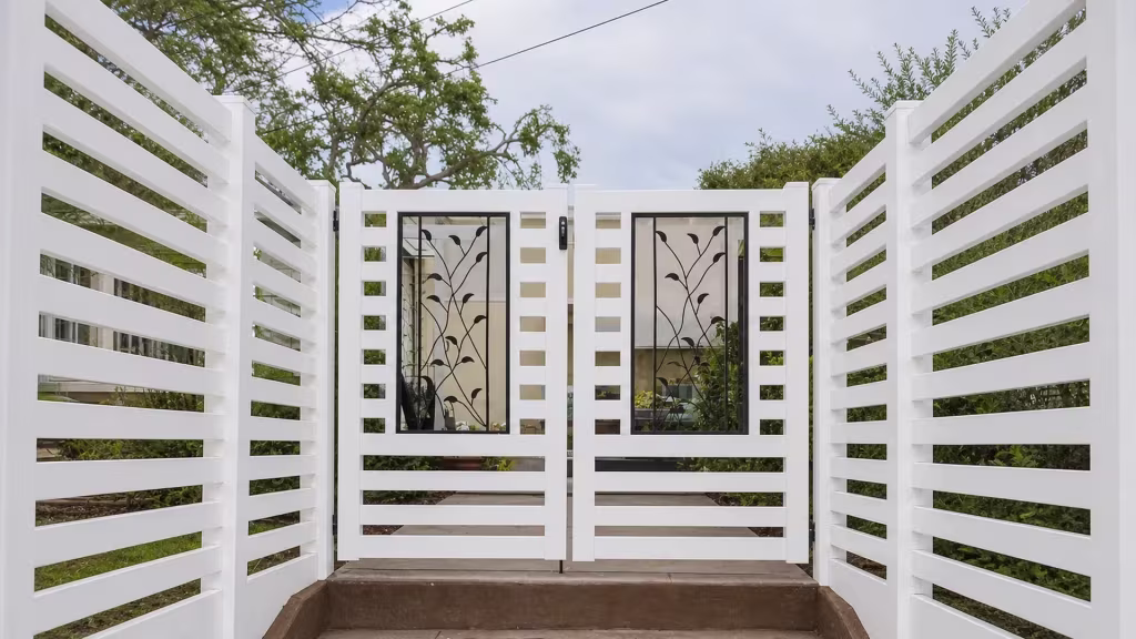 A stepped concrete landing leads up to this White vinyl driveway gate at the top of the walkway