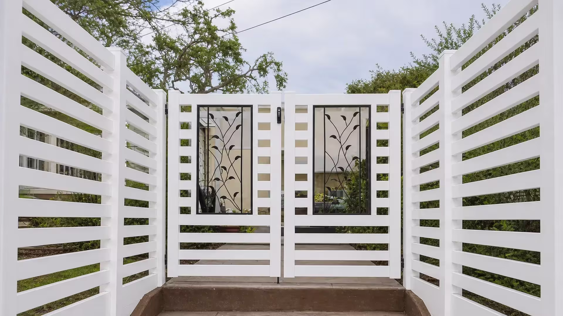 A stepped concrete landing leads up to this White vinyl driveway gate at the top of the walkway