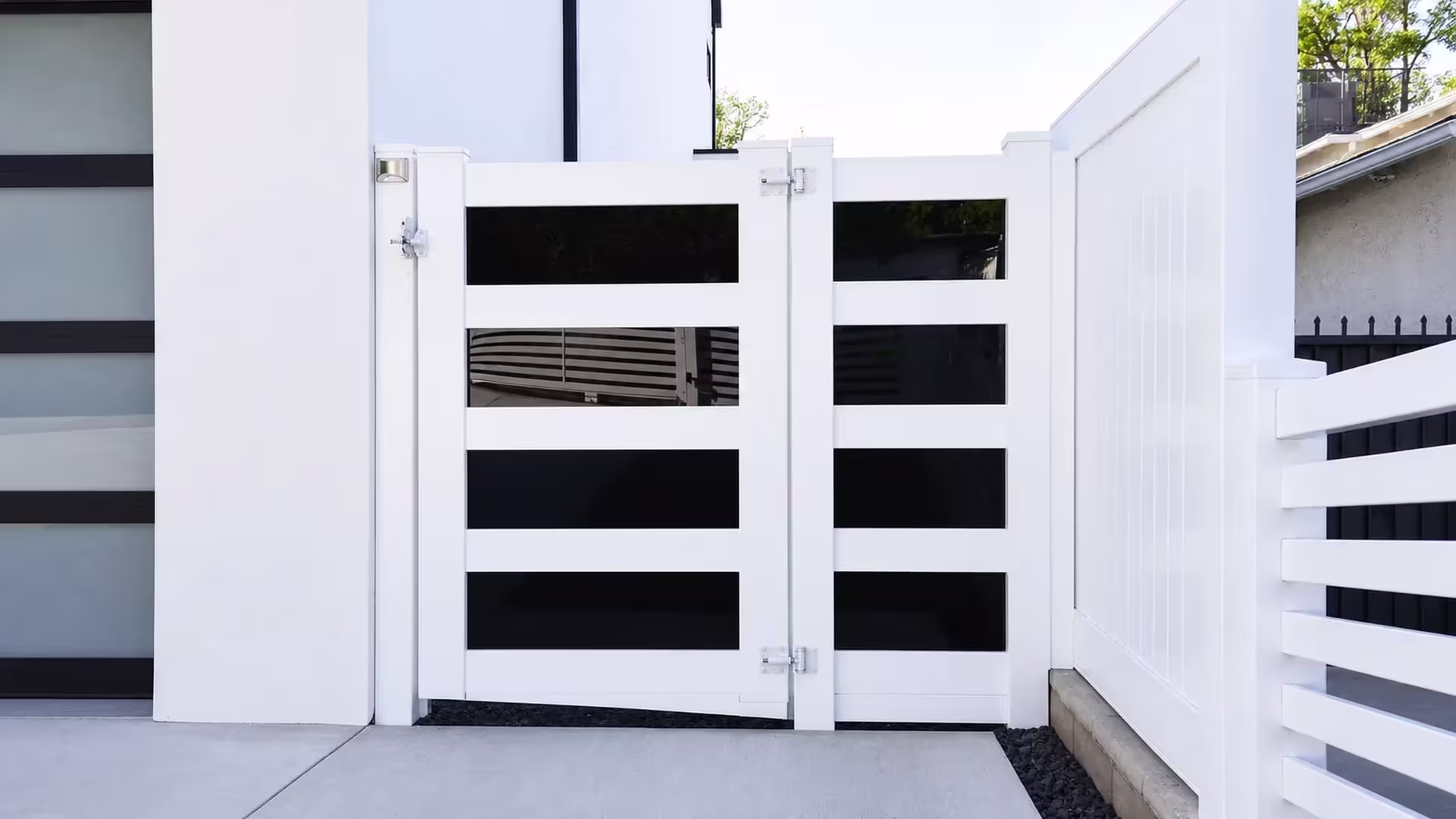 White vinyl driveway gate continuing into a matching privacy fence run beside a raised masonry edge