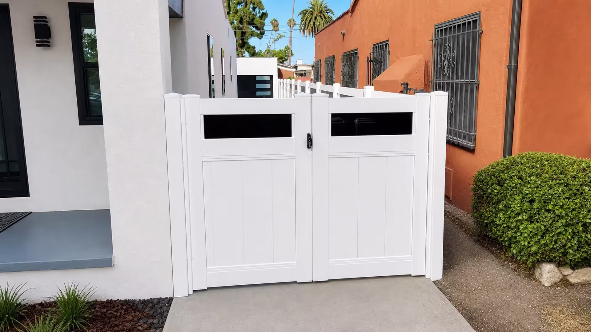 Barred windows mark the terracotta stucco building beside this White vinyl driveway gate with black acrylic inserts