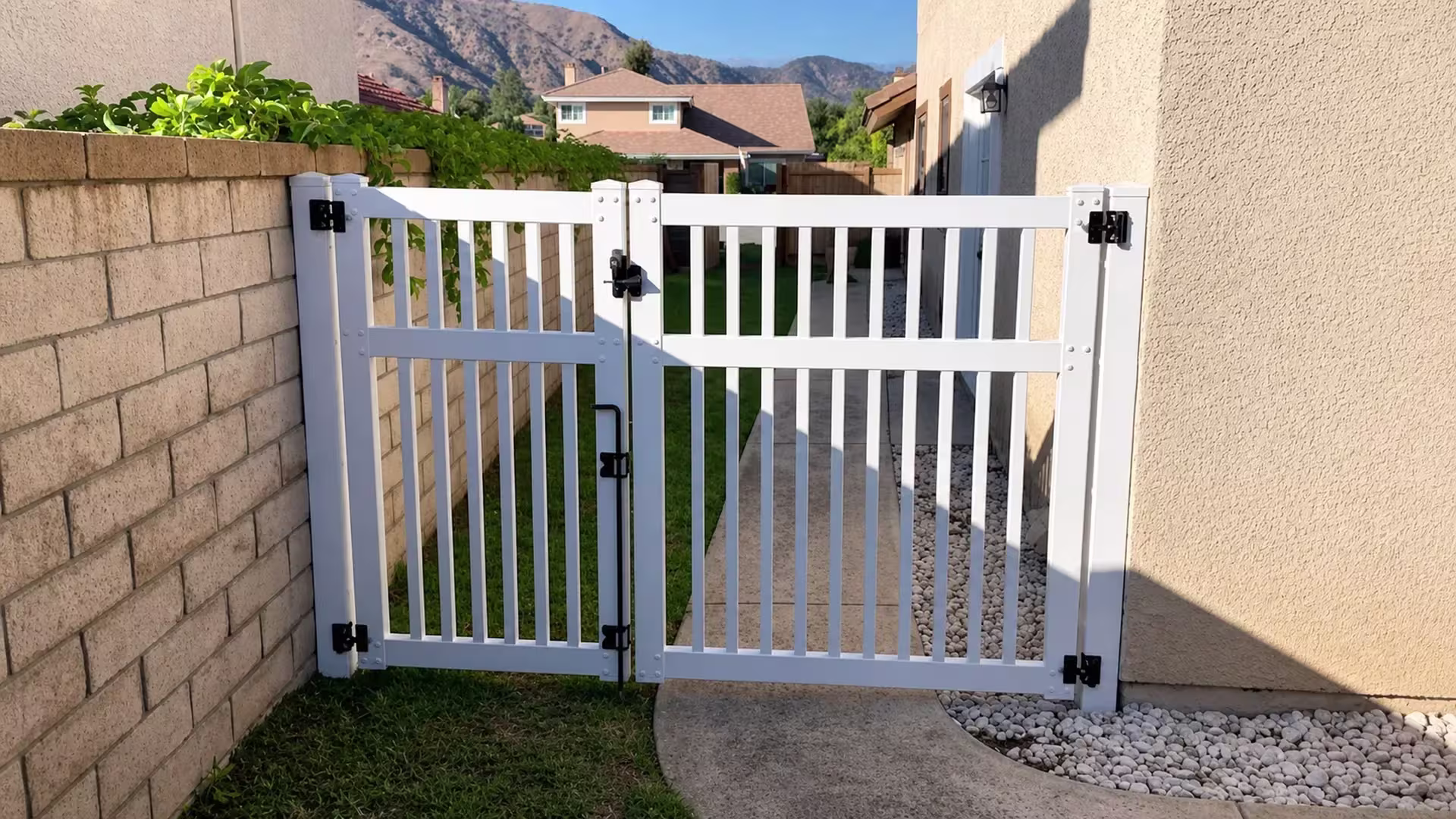 A decorative rock bed lines the walkway beside this White vinyl asymmetrical picket driveway gate