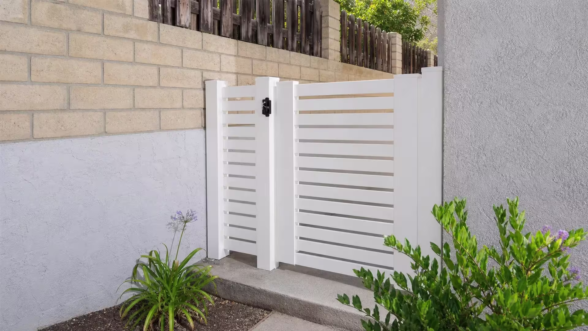 Two unequal White vinyl driveway gate leaves close a narrow side yard opening, both fitted with horizontal slats