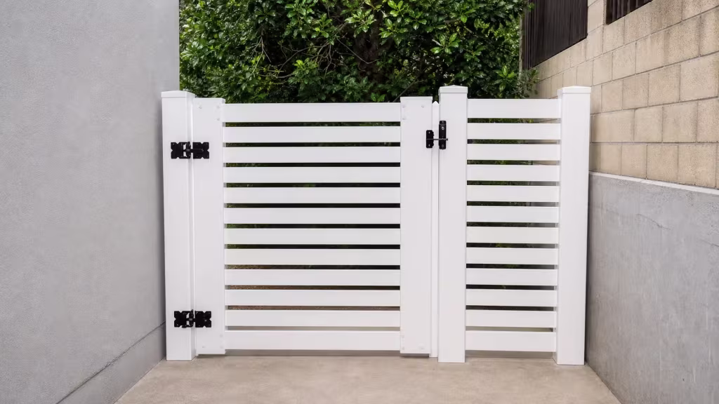 A gray stucco wall and a tan concrete block wall flank this White vinyl driveway gate at a side entry