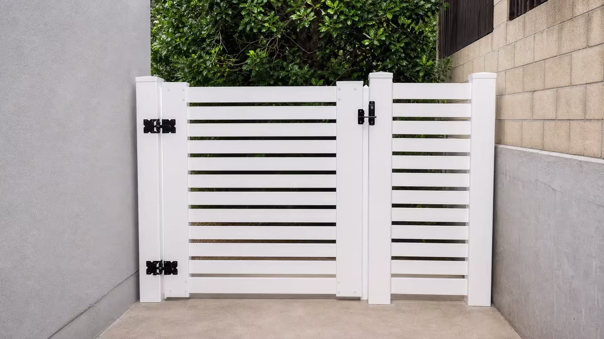 A gray stucco wall and a tan concrete block wall flank this White vinyl driveway gate at a side entry