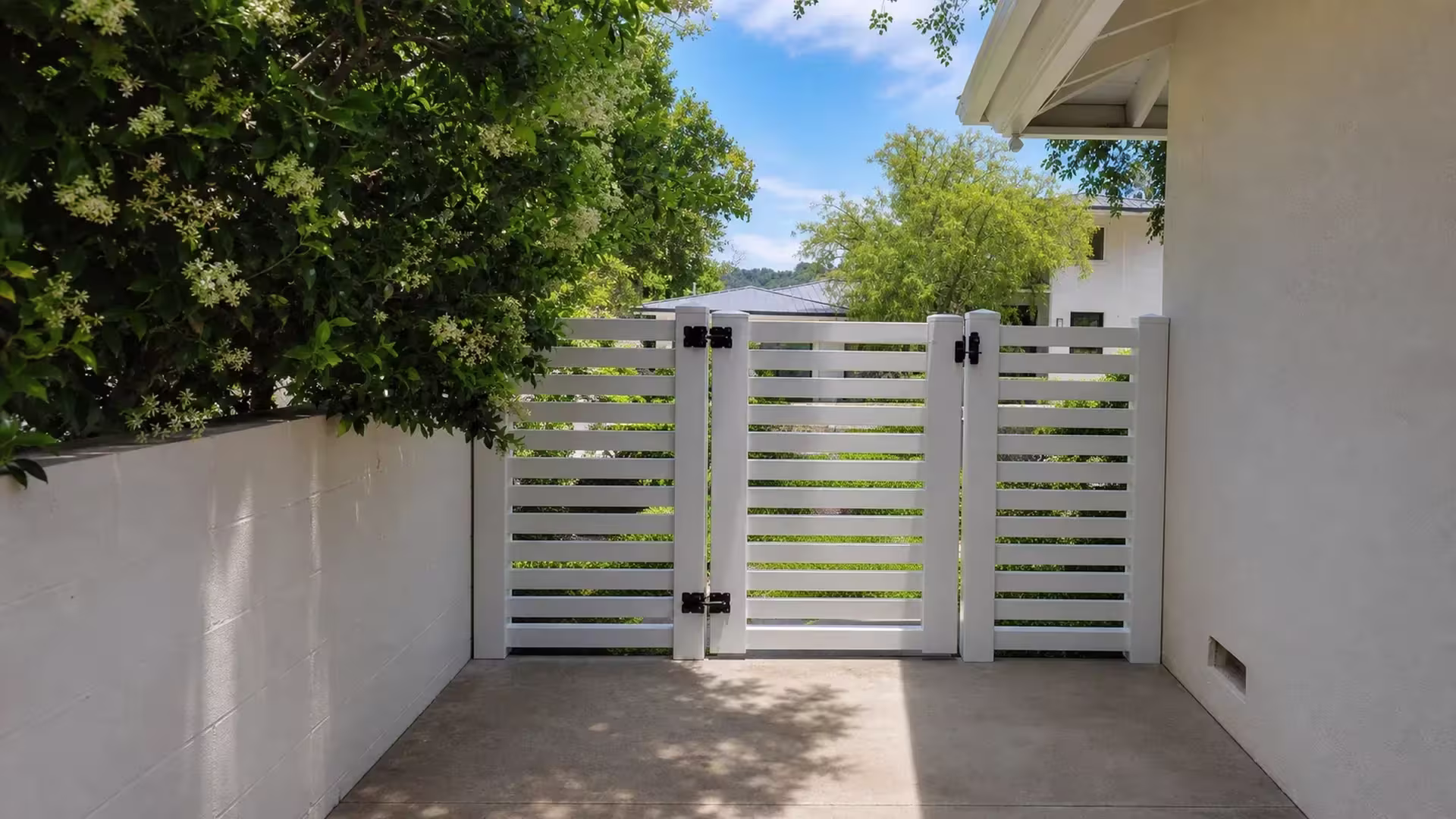 Three horizontal slat sections form this White vinyl driveway gate standing between two stucco property walls