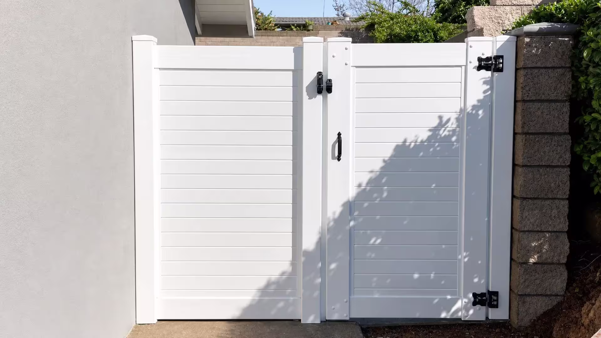 A broad fixed panel and a single swing leaf make up this White vinyl driveway gate beside a masonry column