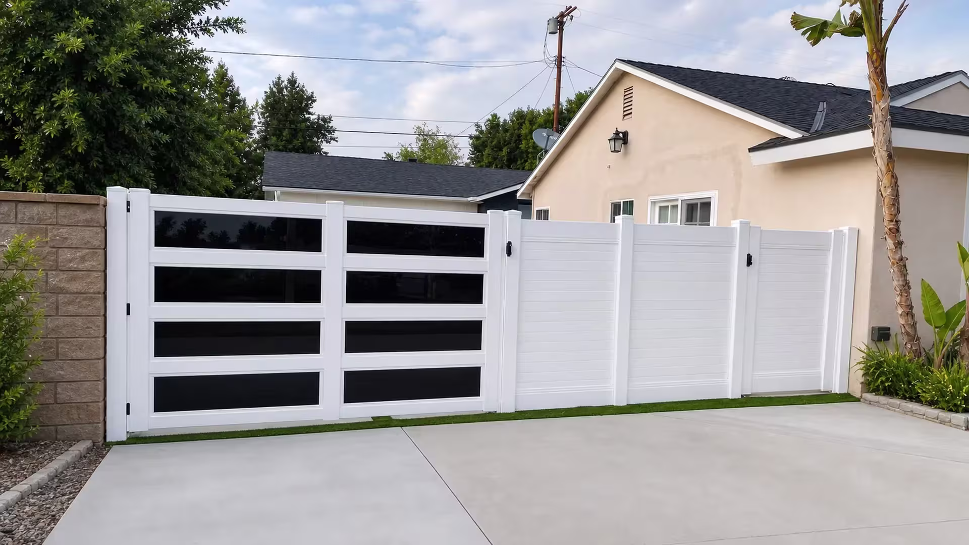 This White vinyl driveway gate carries dark tinted horizontal inset panels across both leaves beside a concrete driveway