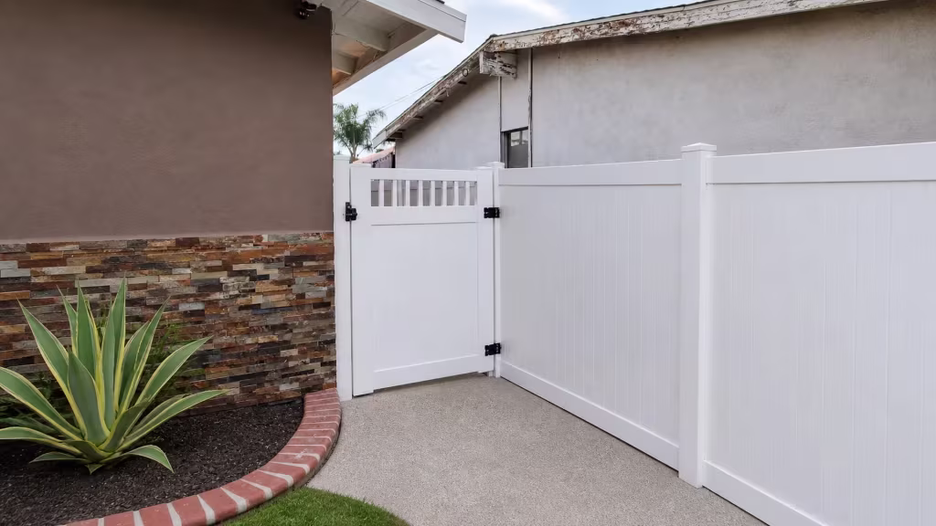 White vinyl gate topped with an open picket band stands between a house wall and stone veneer edging