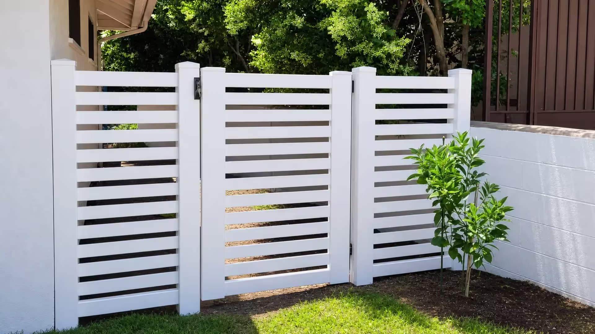 White vinyl gate built with horizontal slats, flanked by a cream building on one side and a brown screened structure opposite
