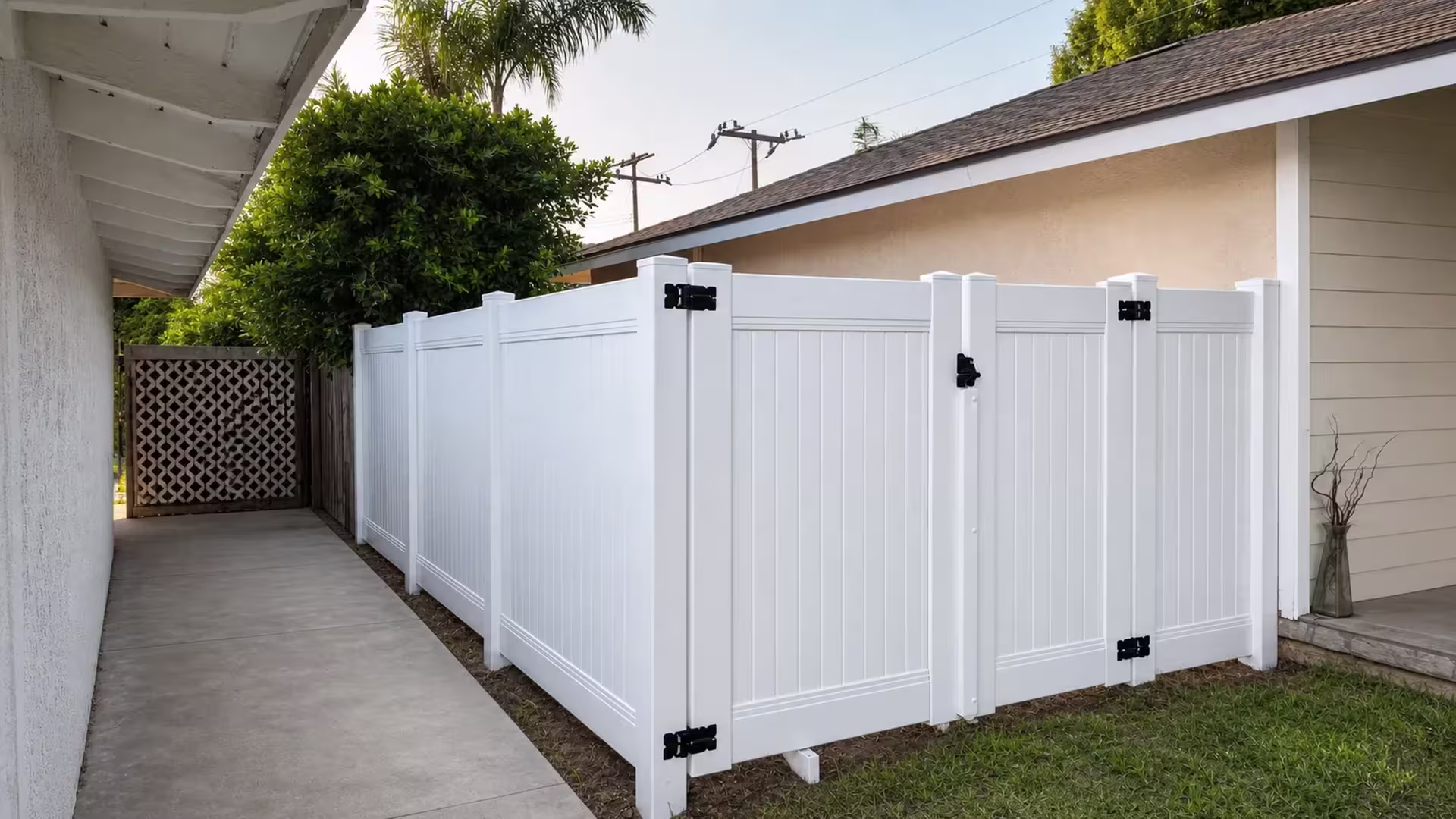 Two White vinyl gate leaves meet at the center of a narrow concrete walkway, secured with black hinge and latch hardware