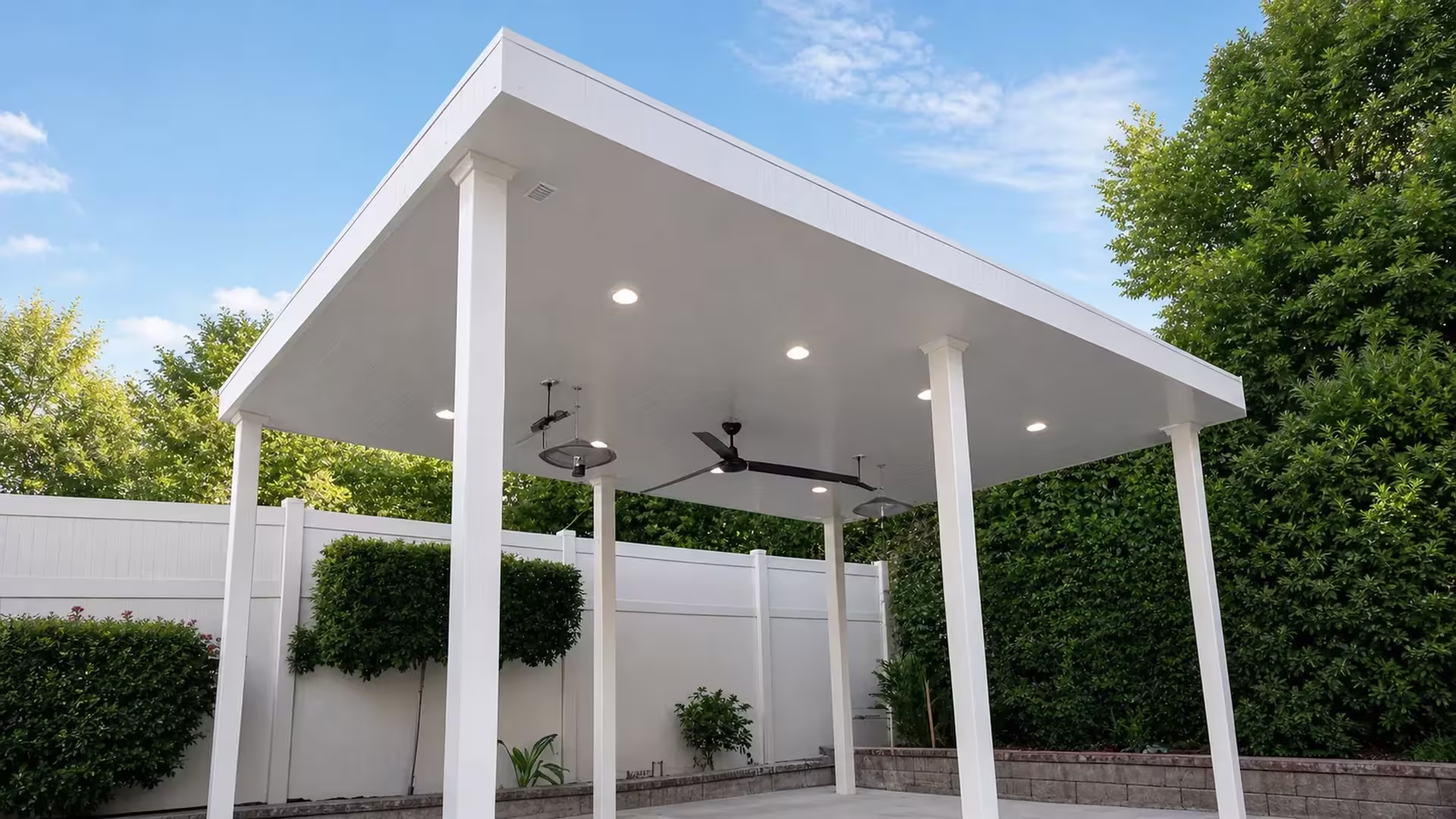 Grooved solid roof underside on a White vinyl freestanding patio cover next to a block retaining wall and fence