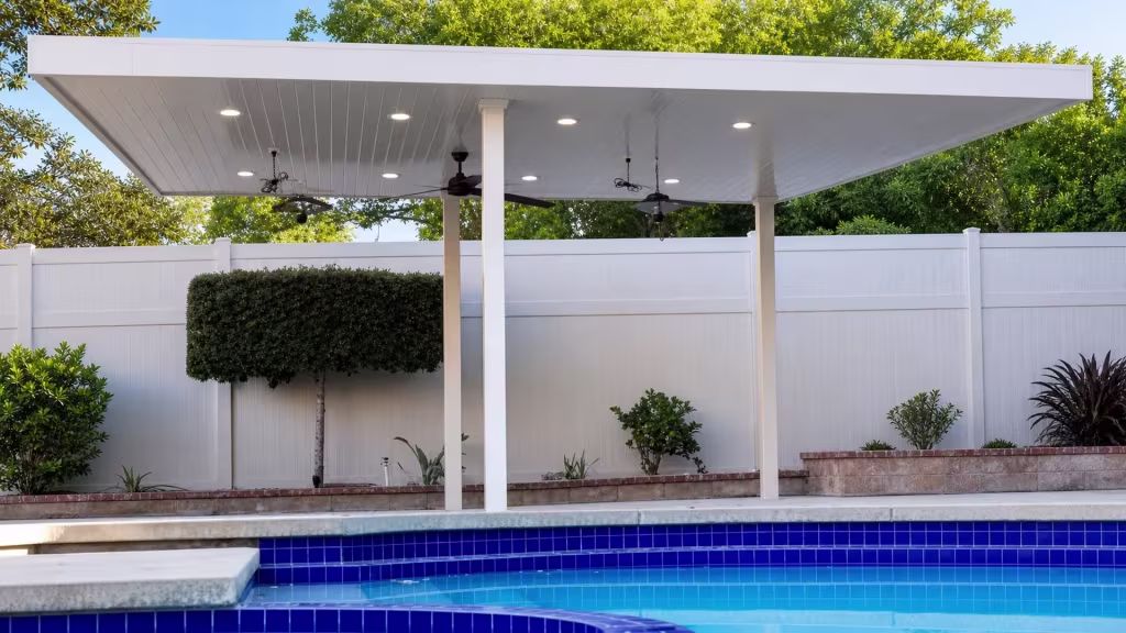 Center White and cream toned posts hold up this freestanding solid roof vinyl patio cover above a blue tiled pool