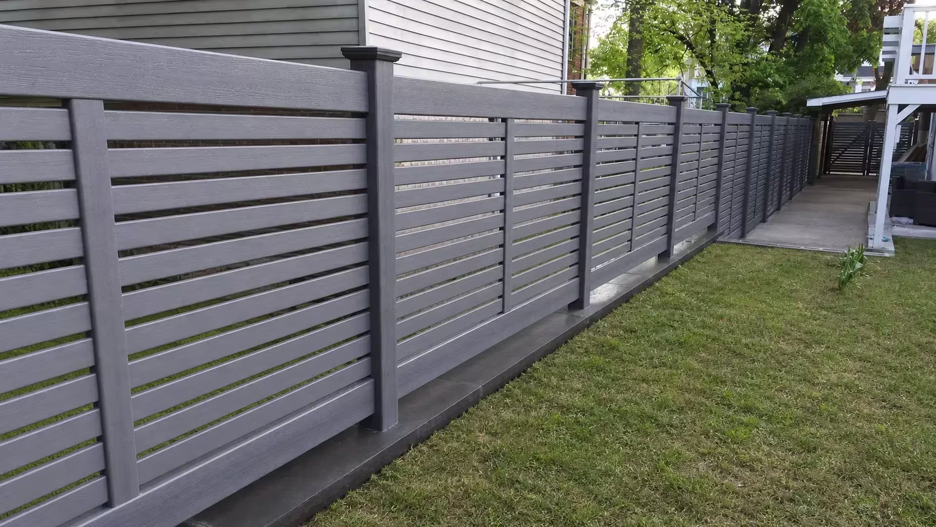 Arctic Blend vinyl picket fence running beside a gray-sided house toward the rear patio deck