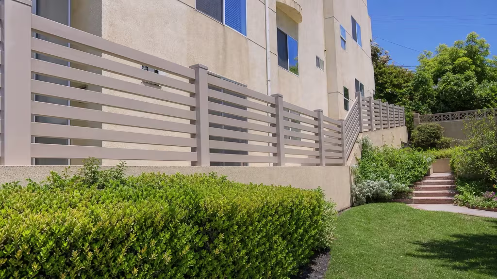 Clay vinyl picket fence following a raised stucco wall past hedges toward a stairway landing