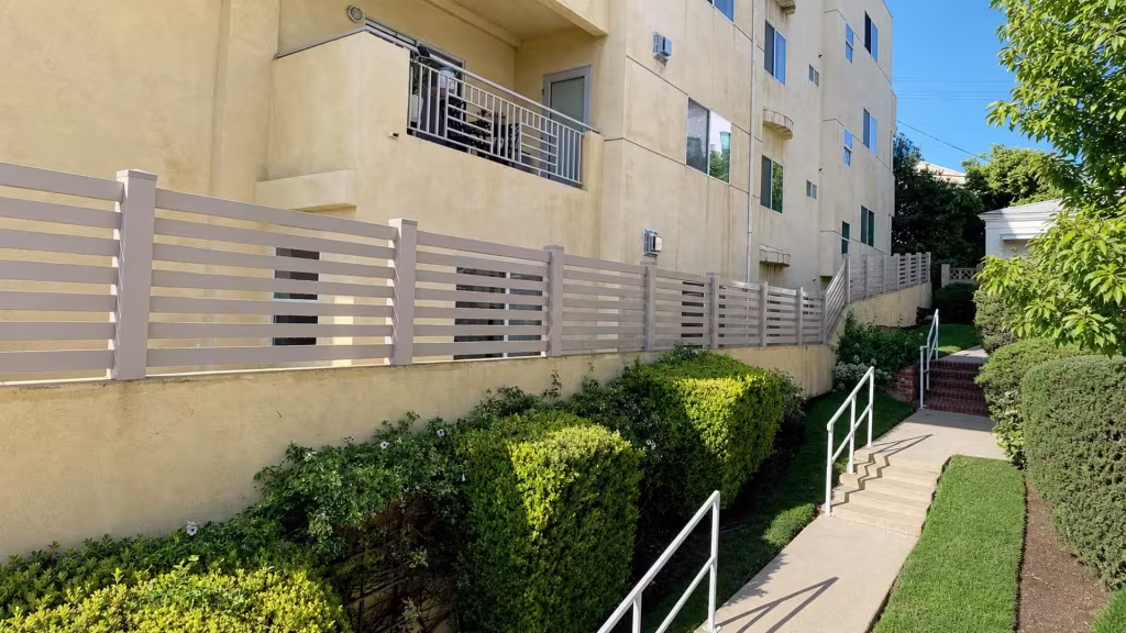 Clay vinyl picket fence stepping up beside a stairway on a sloped stucco retaining wall