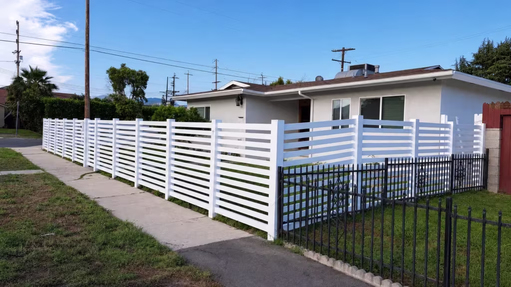 White vinyl picket fence enclosing a front yard that ends near a masonry column and an old wood fence