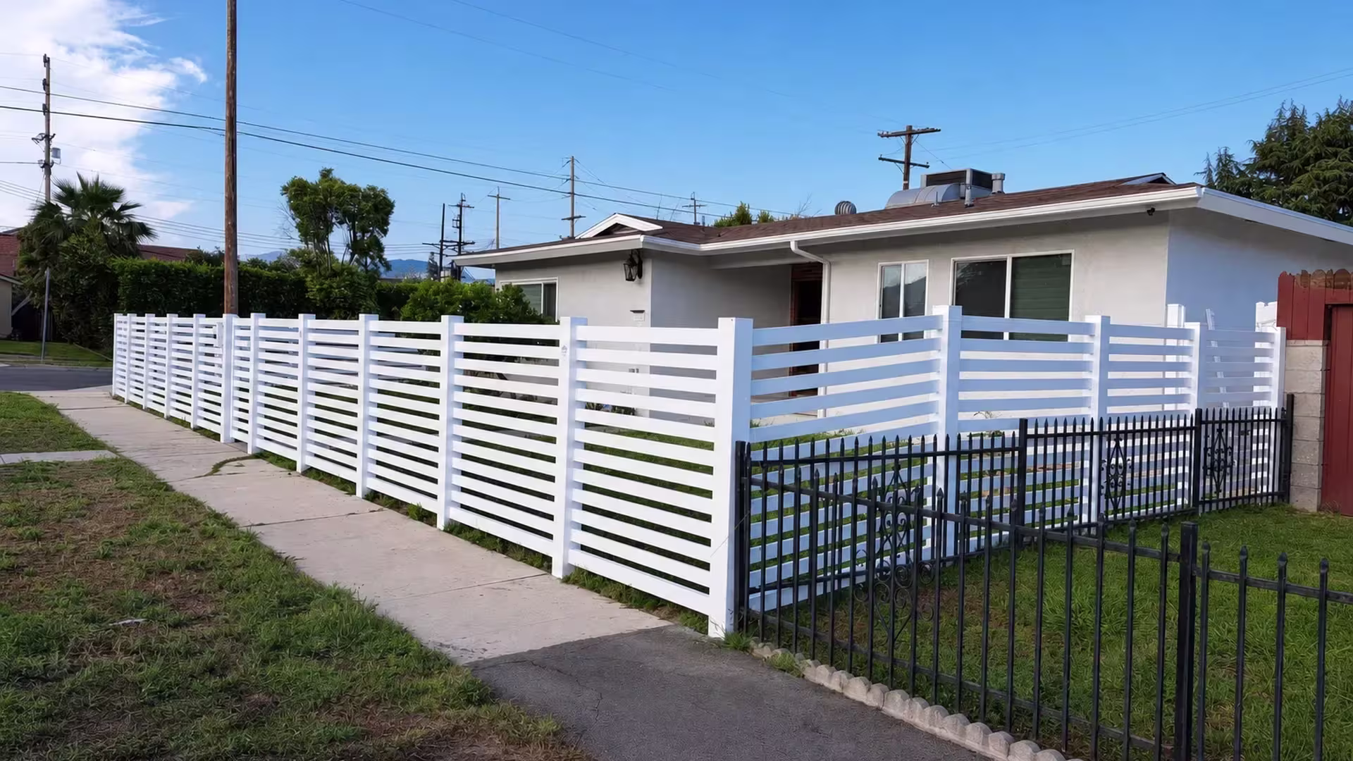 White vinyl picket fence enclosing a front yard that ends near a masonry column and an old wood fence