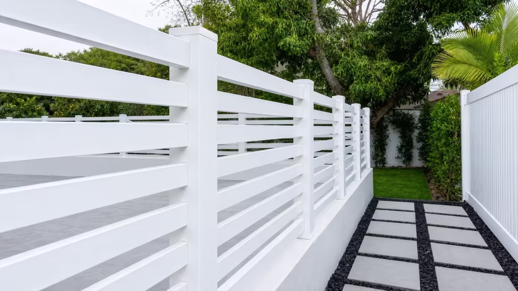 Long White vinyl picket fence tops a low wall beside stepping stones set in dark gravel