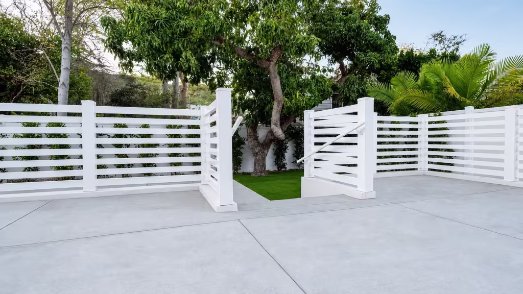 White vinyl picket fence and gate enclosing a concrete patio shaded by mature palms