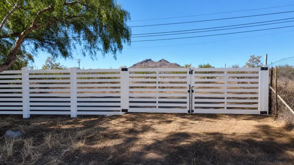 Beneath a mature shade tree, this White vinyl picket fence pairs with a centered double driveway gate
