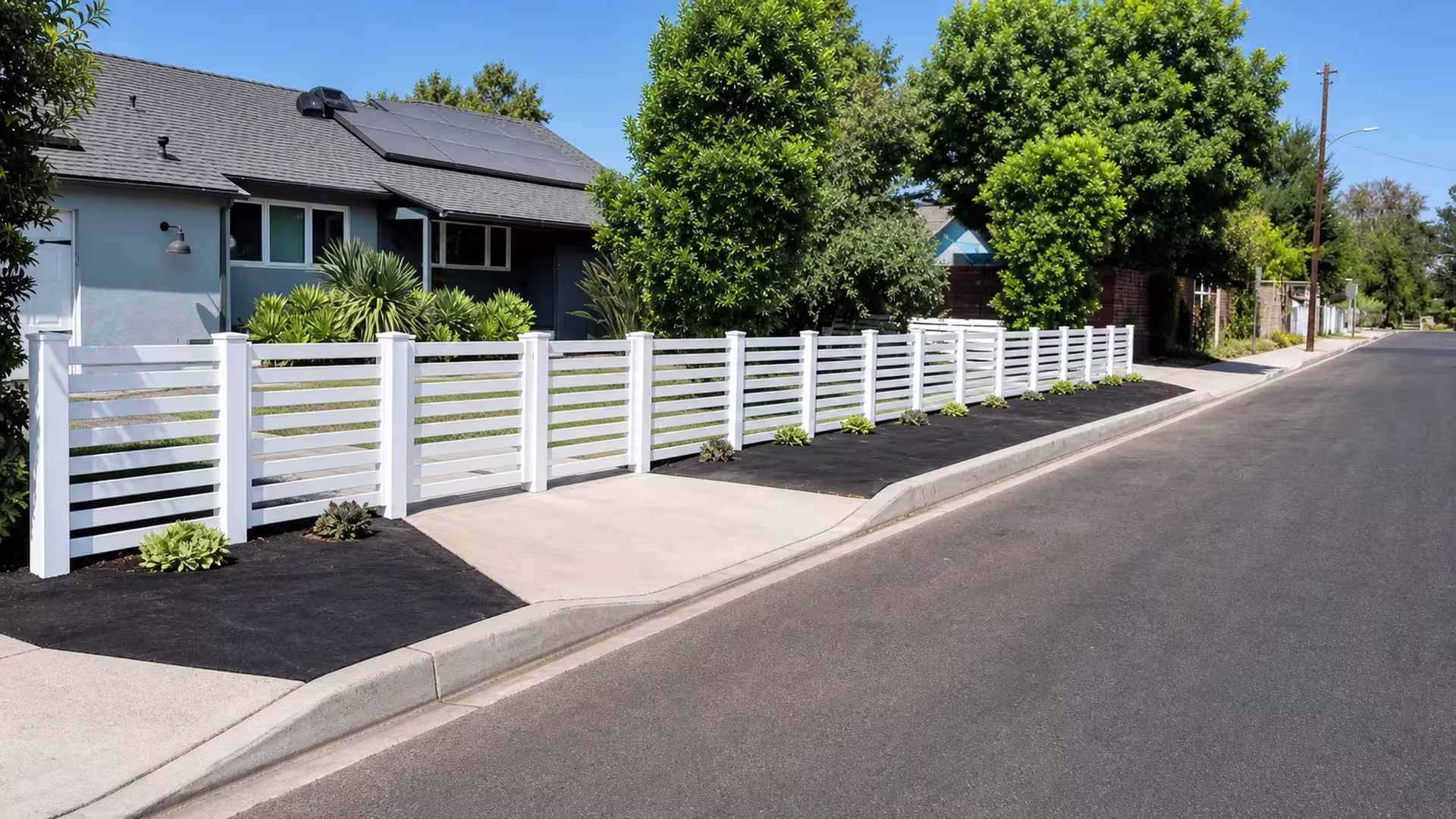 Eleven panel bays of White vinyl horizontal picket fence run the front property line near the curb and street