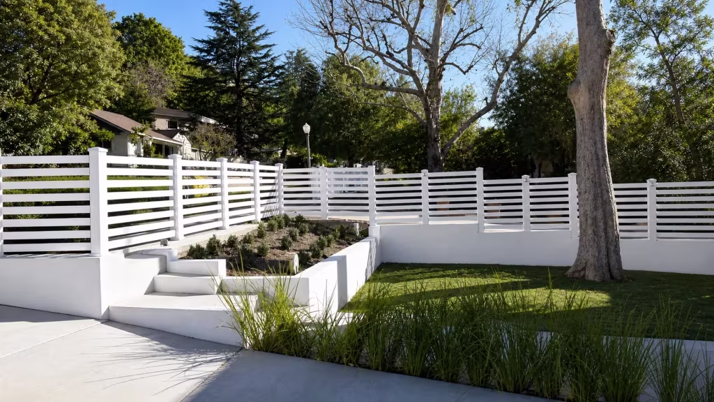 Terraced retaining walls carry this White vinyl picket fence past a lamp post and clipped grasses